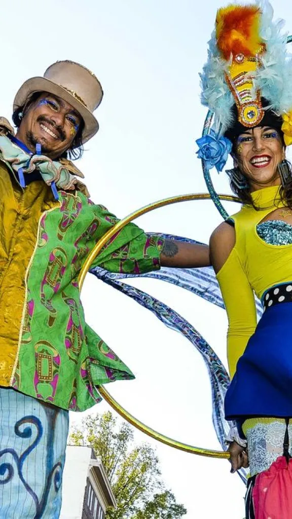 Two stilt walkers in bright, festive costumes holding hula hoops and smiling at Old City Fest