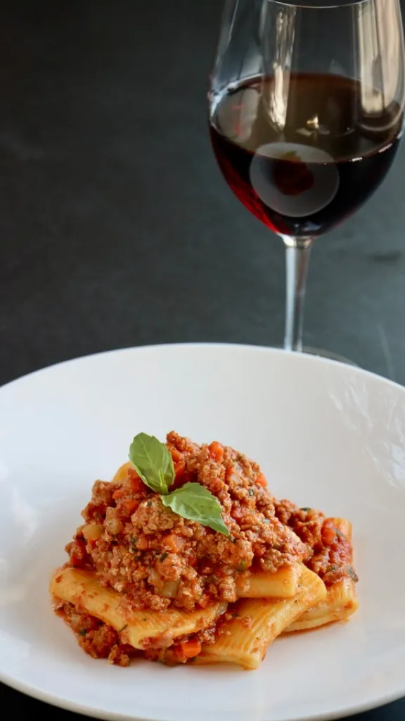 Rigatoni on a plate with a glass of wine