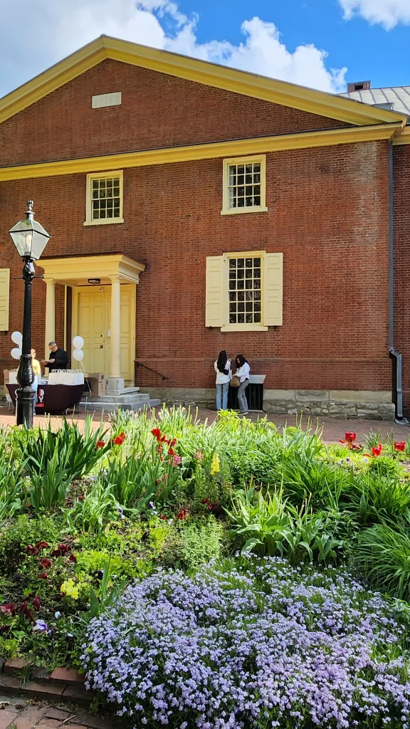 Red brick Quaker meetinghouse with grass and flowers in the foreground.