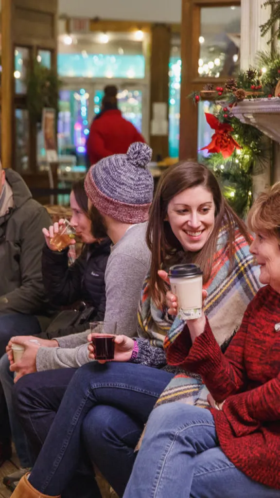 Photo of people sitting inside a cozy, winter-themed lounge and enjoying beverages while conversating. 
