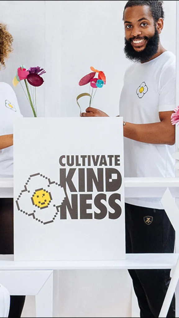 People holding colorful  paper flowers in a white market stand made out of cardboard.