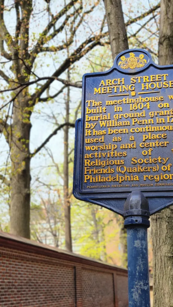 Blue historic marker for Arch Street Meeting House. Marker reads, "The meetinghouse was built in 1804 on a burial ground granted by William Penn in 1701. It has been continuously used as a place of worship and center for activities of the Religious Society of Friends (Quakers) of the Philadelphia region.   Erected 1954 by Pennsylvania Historical & Museum Commission."