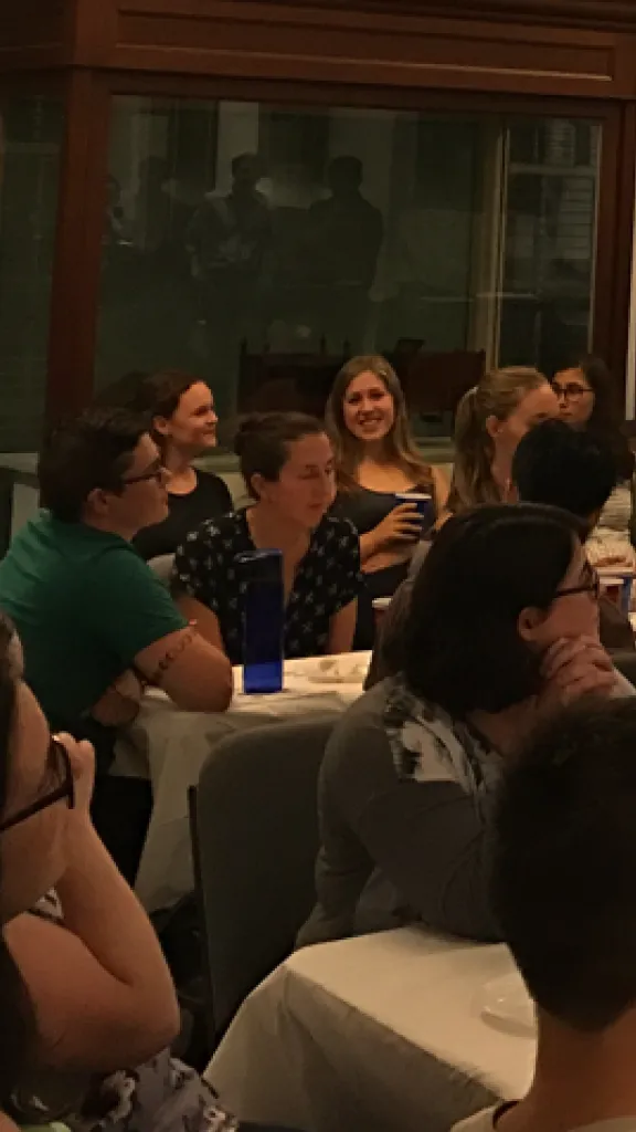 people sitting at tables in groups in a room looking towards the front