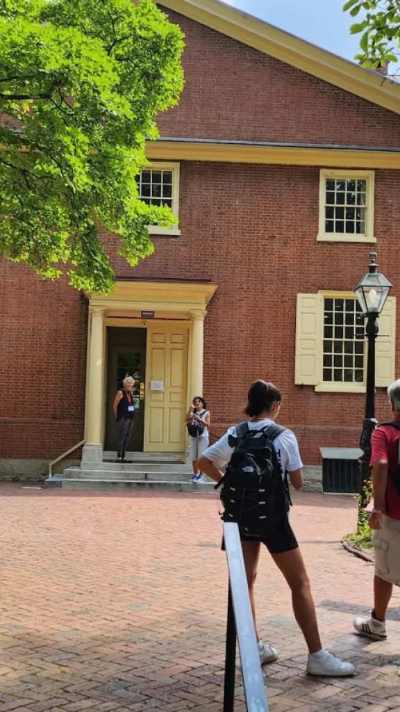 Two people walk up a brick path toward a large brick Quaker meetinghouse with an entrance door.