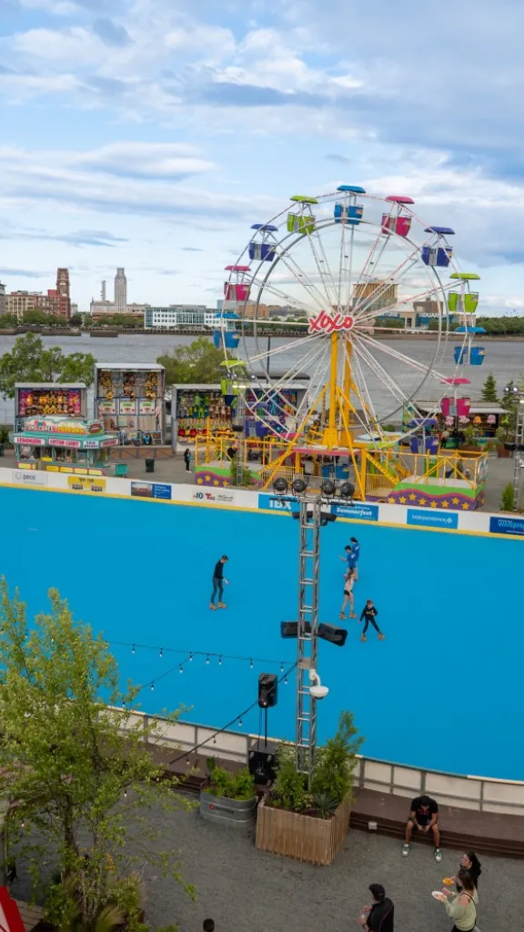 View of Independence Blue Cross RiverRink with skaters on the rink, the Ferris wheel, and the Delaware River in the background.