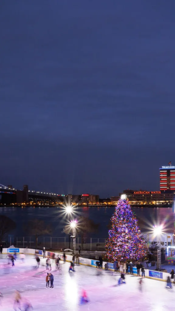 Overlooking Independence Blue Cross RiverRink during winter season all lit up with Ben Franklin Bridge in the background.