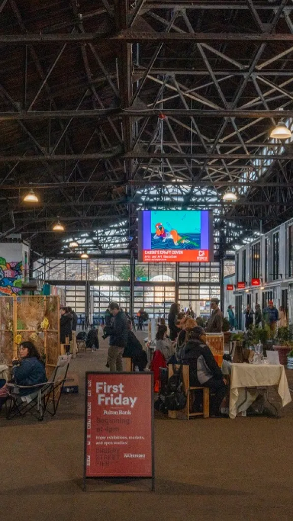 Inside of Cherry Street Pier hosting First Friday event with a sign in the middle and a market of vendors and shoppers.