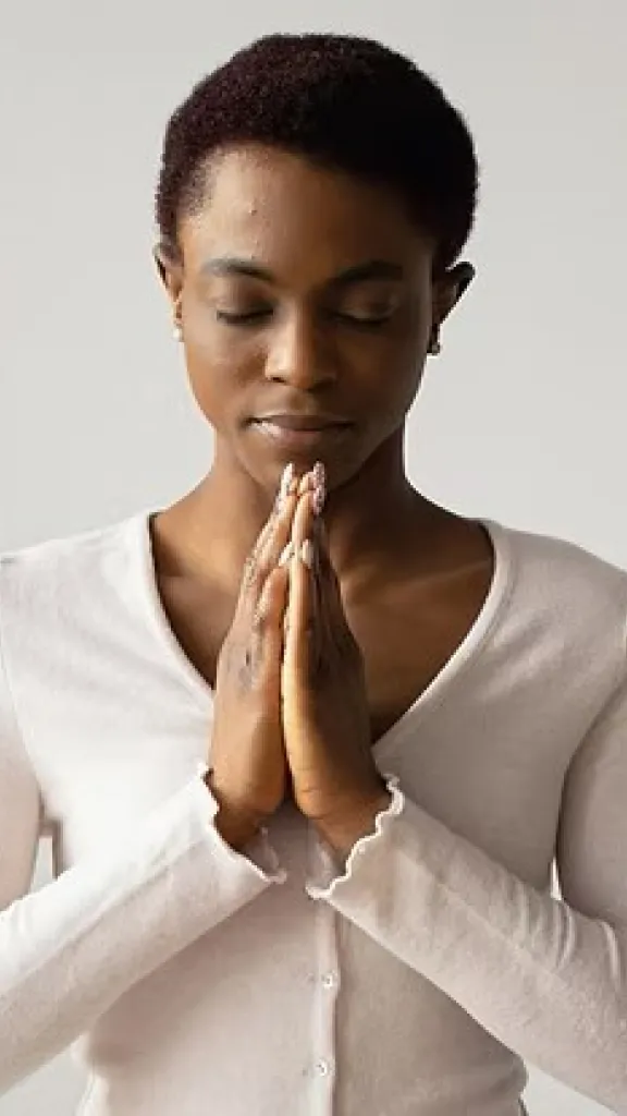 A woman in a white shirt with her hands at her heart in meditation or prayer