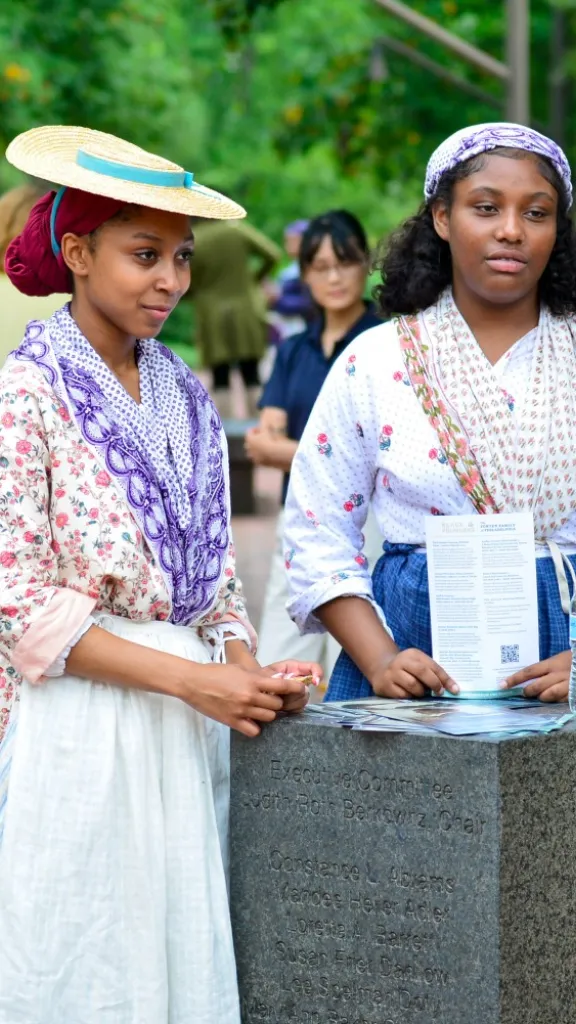 Two women in 18th century clothing speaking with person in modern clothing