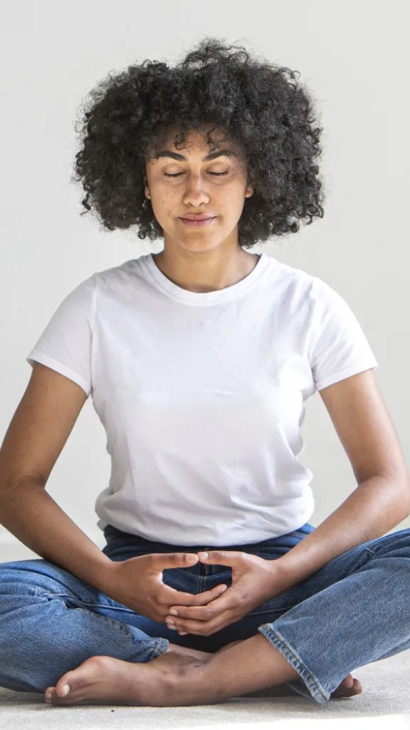 A woman in a white shirt with her hands at her heart in meditation or prayer