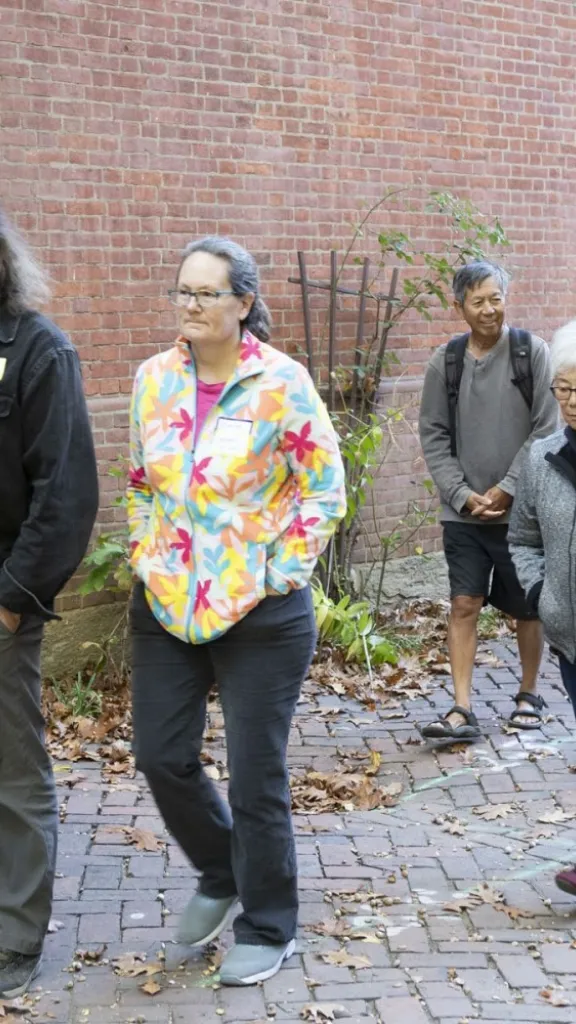 Group of adults walking outdoors along the exterior redbrick wall of Arch Street Meeting House