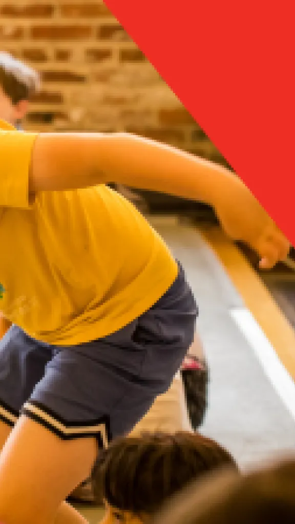 A boy in a yellow shirt getting up off the floor to run across the room. Text that reads "Play-in-a-Day" and "Grades K-5"