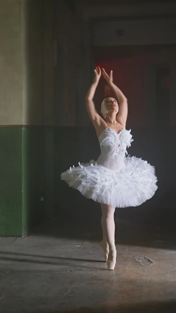 Ballernia wearing a white costume dances in a dark hallway