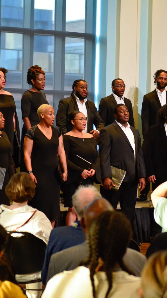 Chorale of men dressed in suits and women dressed in black dresses sing