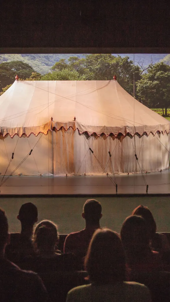 People sitting in a theater looking at Revolutionary-era war tent behind