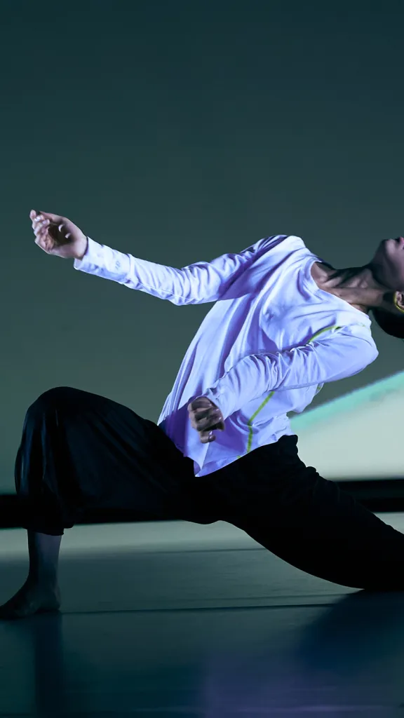 Dancer sits in a deep lunge, arms extended out and head released to the sky.