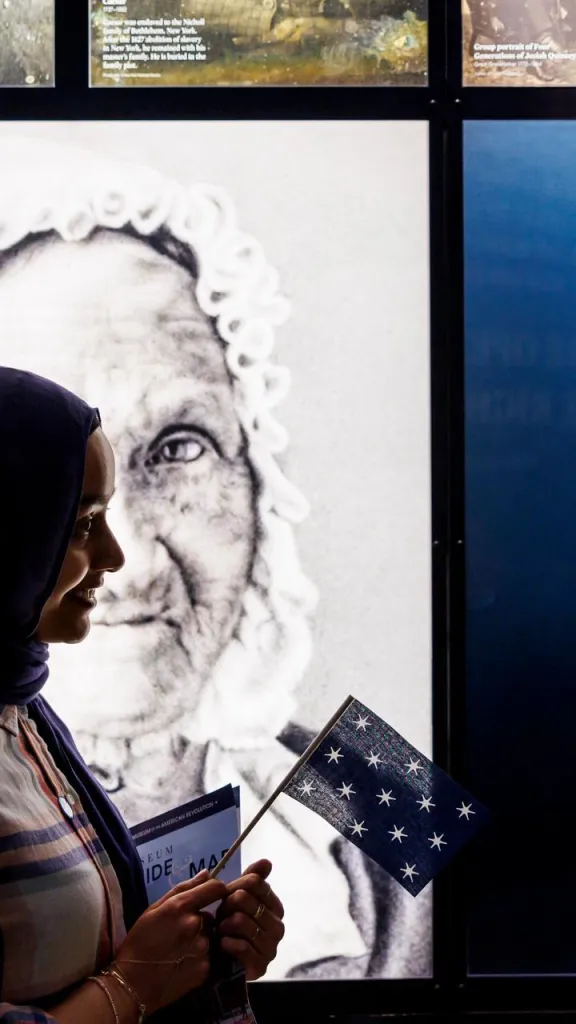 Woman with a hijab holding a colonial-era flag in front of 19th-century photo