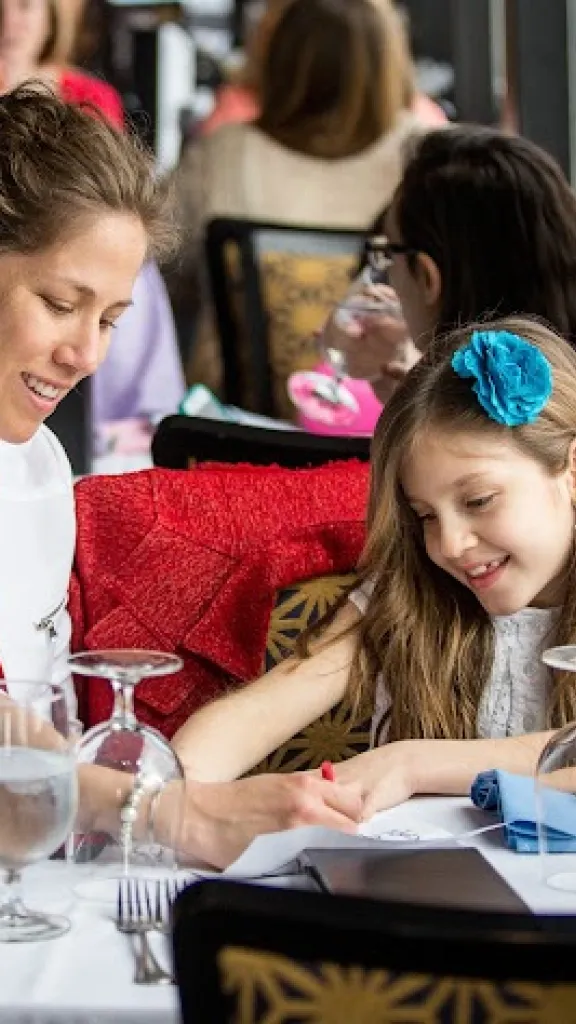 Mother and daughter sharing a coloring book at a dinner table together 