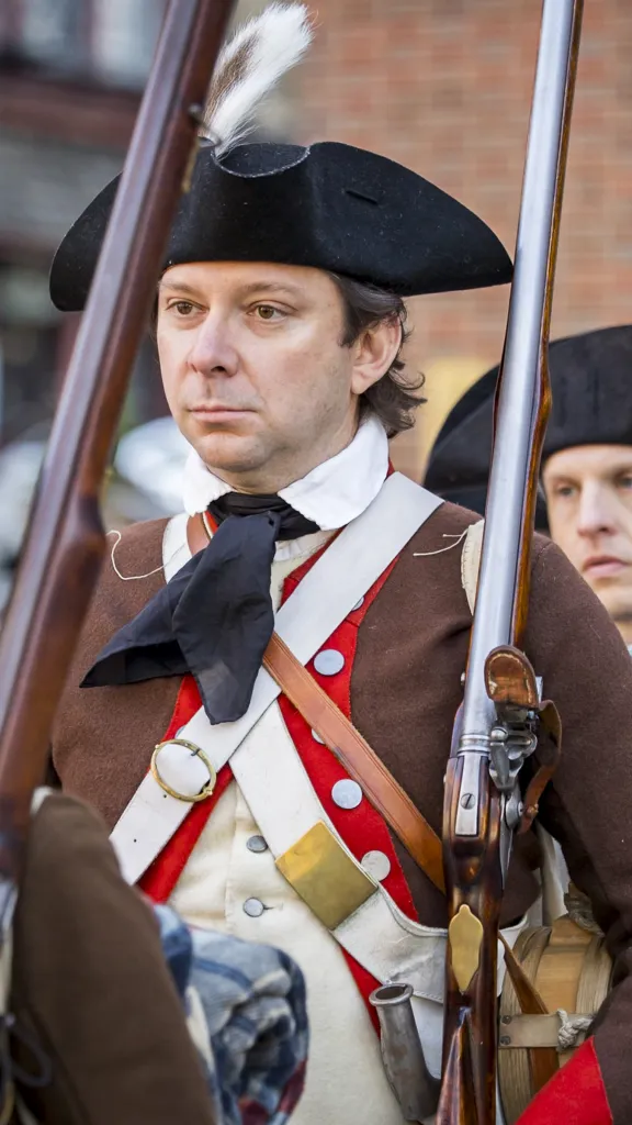 men wearing tricorn hats and brown coats holding revolutionary era rifles