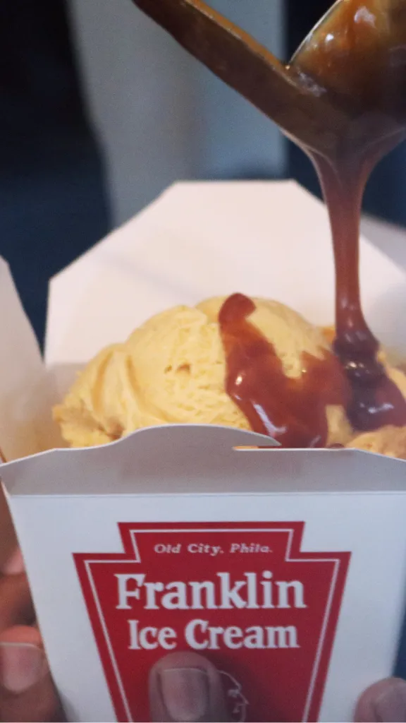 caramel sauce being drizzled over a scoop of ice cream in a Franklin Ice Cream container