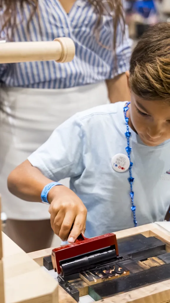 Boy uses ink sponge roller over printing press typeset