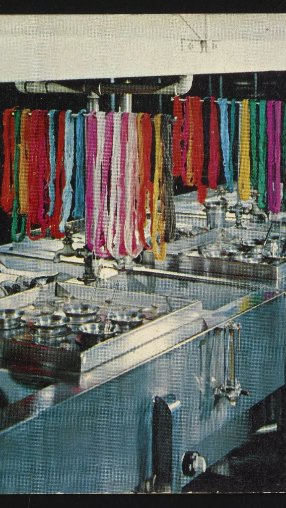 Postcard for General Dyestuff Corporation depicting a worker using a dye bath with colorful strands of fabric draped above the baths, ca. 1953.