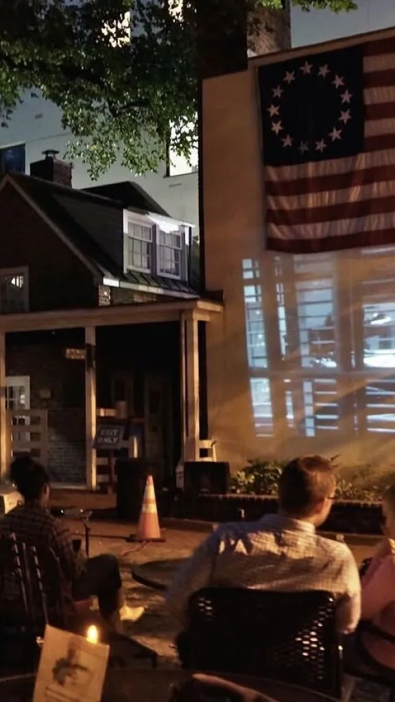 group watching movie projected onto outside wall of betsy ross house under the flag