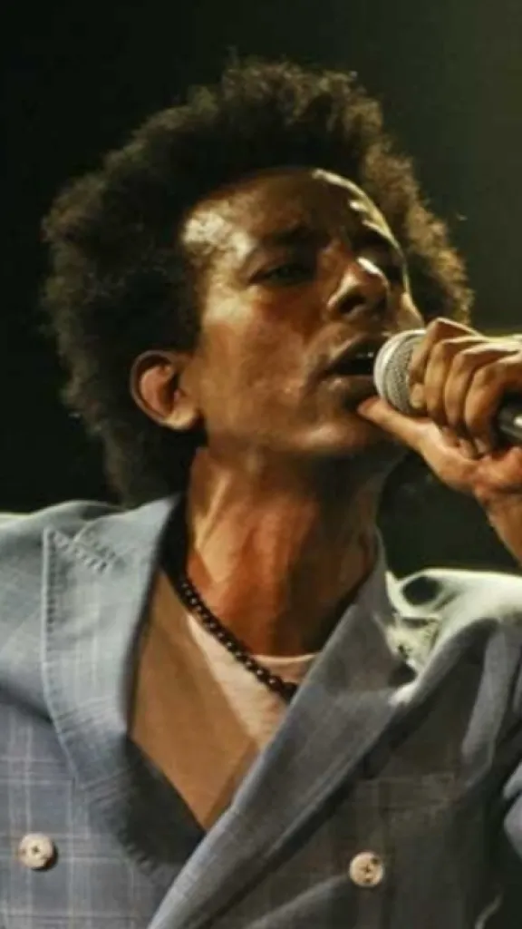 photo of black man with afro holding a microphone to his mouth and wearing a light blue suit