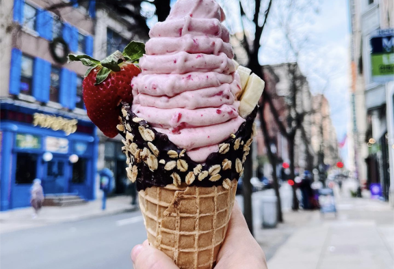 Person holding up strawberry soft serve ice cream with chocolate dipped cone