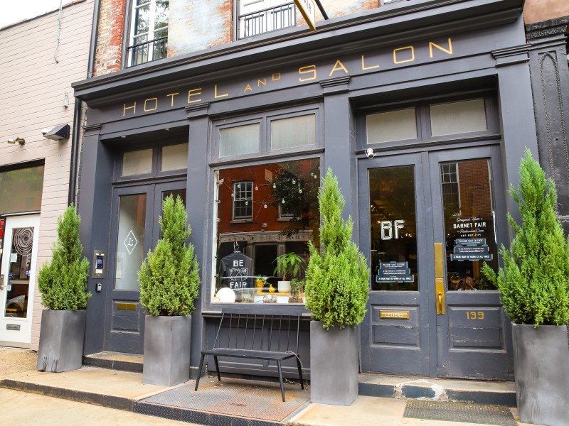 Gray exterior of Lokal Hotel and Barnet Fair along N. 3rd Street in Old City, with four large plants outside salon.