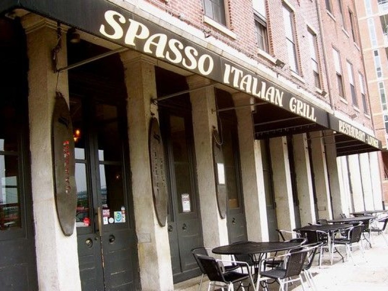 Exterior of Spasso Italian Grill showing front door, outdoor seating, and black awning with restaurant name printed in white