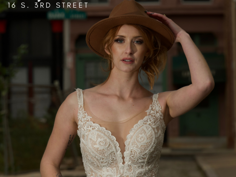 Person wearing white bridal gown and brown hat with text in top right corner of business name and address