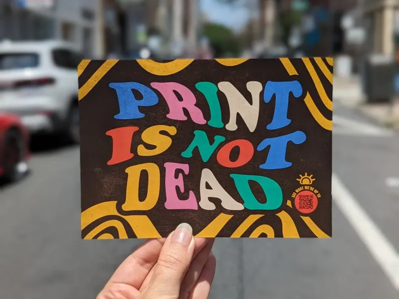 Person holding flyer that says "Print is not dead"