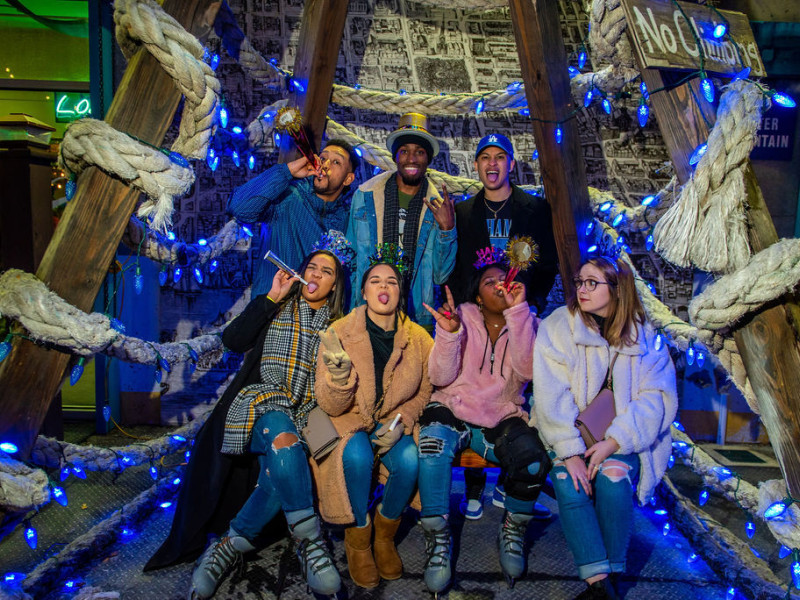 Group of 7 mixed gender/race people posing smiling, laughing and celebrating New Year's with party favors. 