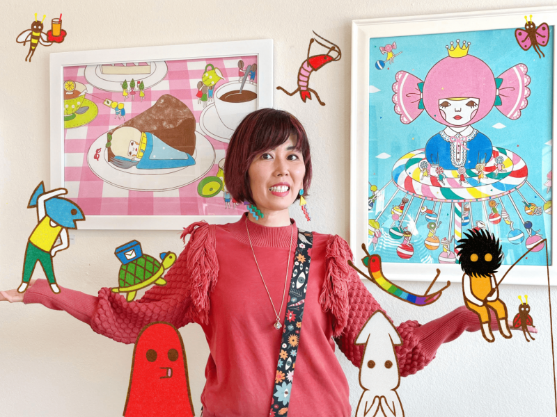 Photo of artist Naoshi with two framed pieces of art hanging on a wall behind her, cartoon characters surround her face 