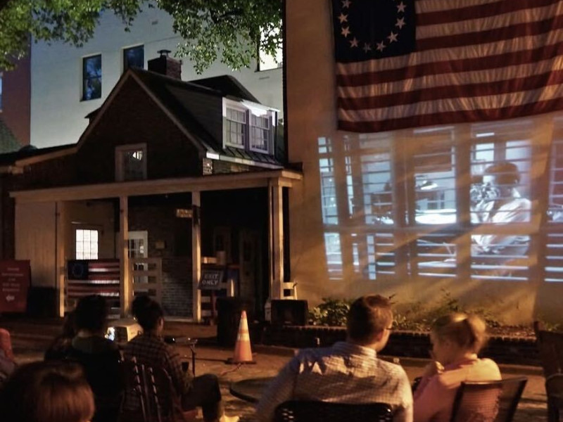 group watching movie projected onto outside wall of betsy ross house under the flag