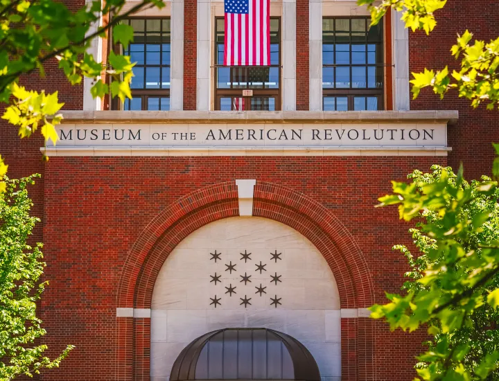 Front entrance of the Museum of American Revolution with American Flag above doorway and trees in foreground
