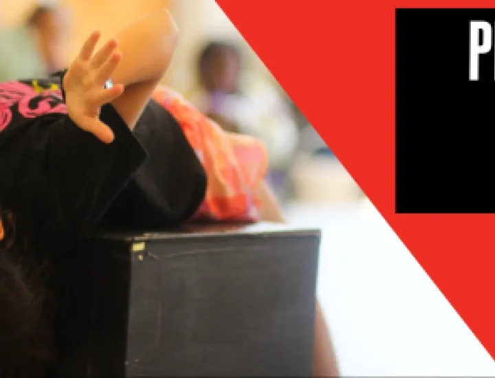 A child leans upside down over the top of a black box and splays their hands out forward. Text that reads "Play-in-a-Day" and "Grades K-5"