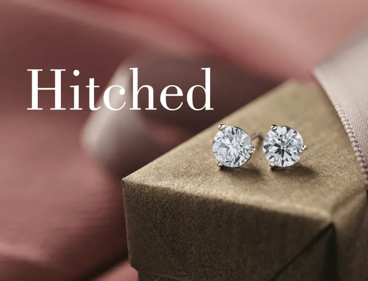 A pair of diamond studs sitting on a green gift box and surrounded by pink fabric and ribbon