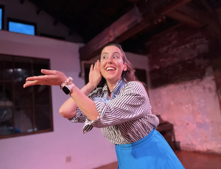 Lee Minora smiling, she gestures animatedly with one hand cupped to her ear and the other extended outward.