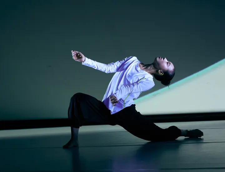 Dancer sits in a deep lunge, arms extended out and head released to the sky.