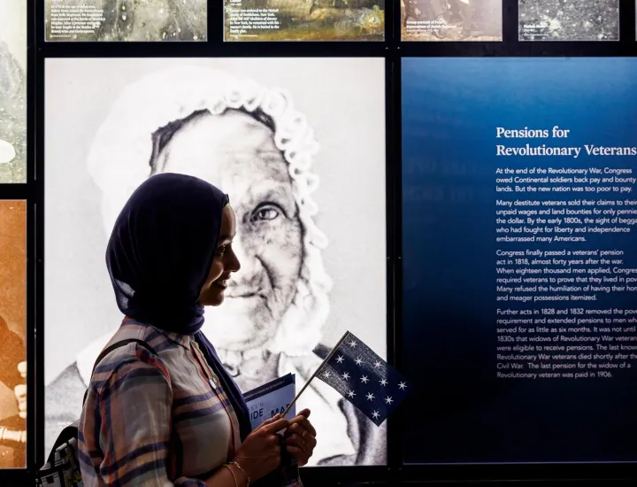 Woman with a hijab holding a colonial-era flag in front of 19th-century photo