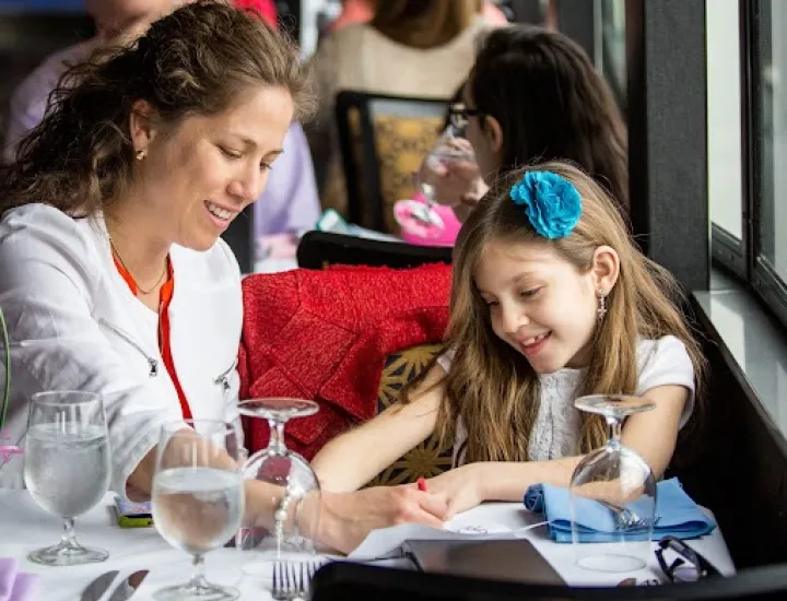 Mother and daughter sharing a coloring book at a dinner table together 