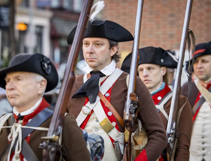 men wearing tricorn hats and brown coats holding revolutionary era rifles