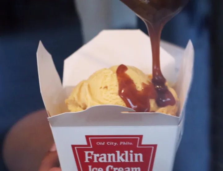 caramel sauce being drizzled over a scoop of ice cream in a Franklin Ice Cream container