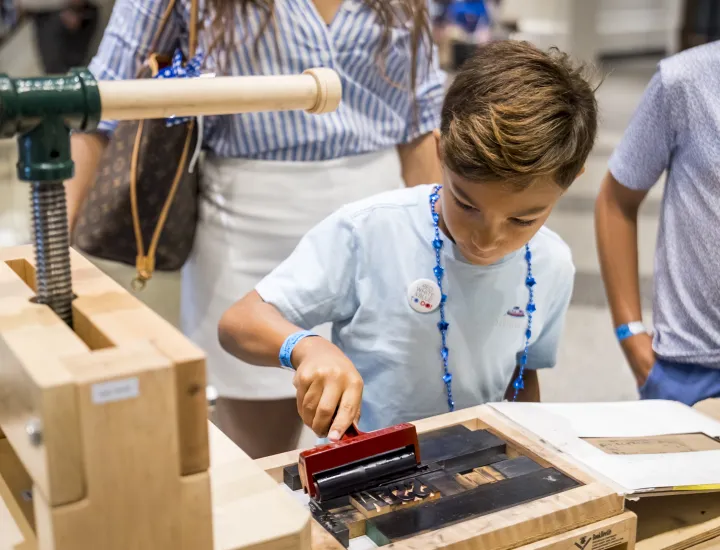 Boy uses ink sponge roller over printing press typeset
