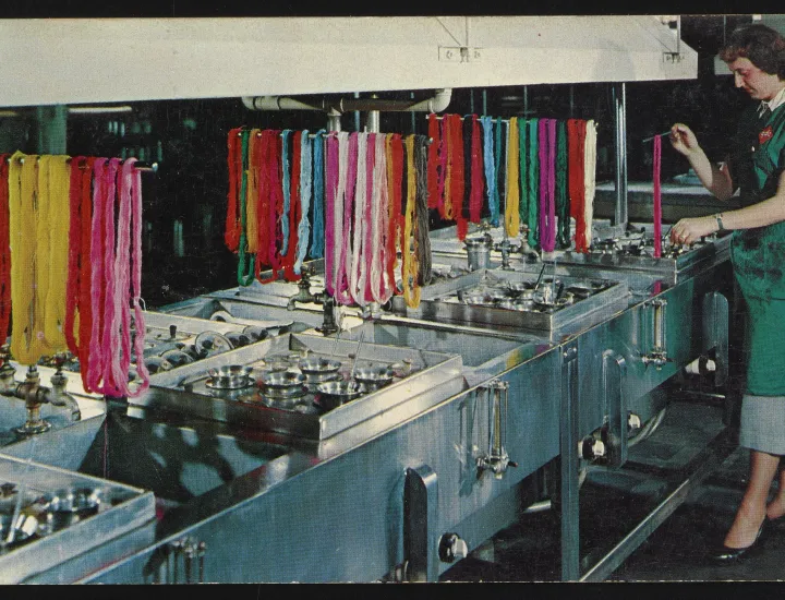 Postcard for General Dyestuff Corporation depicting a worker using a dye bath with colorful strands of fabric draped above the baths, ca. 1953.
