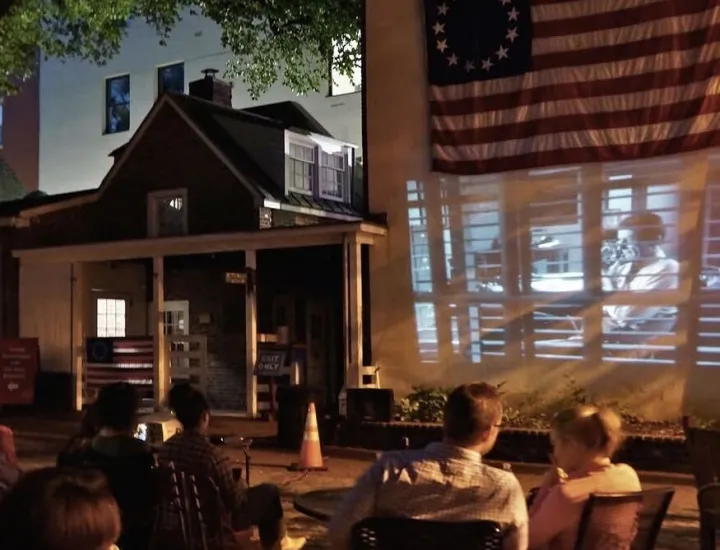 group watching movie projected onto outside wall of betsy ross house under the flag