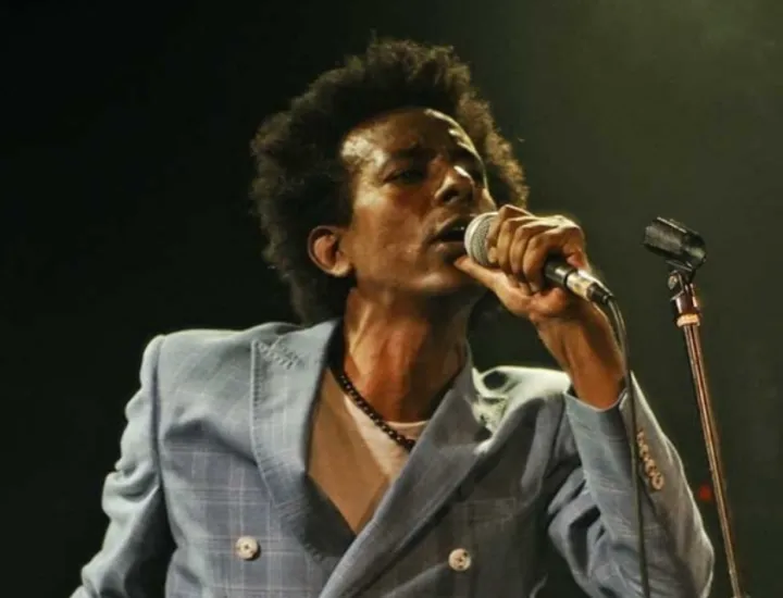 photo of black man with afro holding a microphone to his mouth and wearing a light blue suit